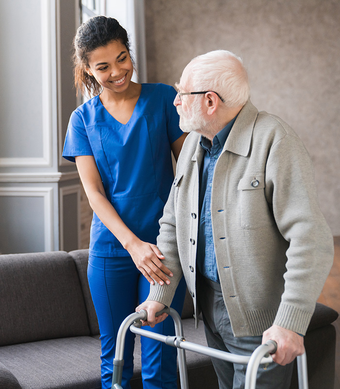 a caregiver with an elderly man using a walker in his home